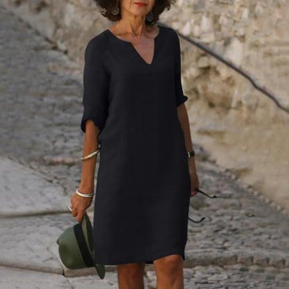 Woman in a black dress holding a green hat on a stone path.