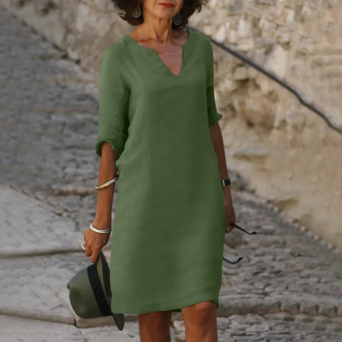 Woman wearing a green dress holding a hat on a stone path.