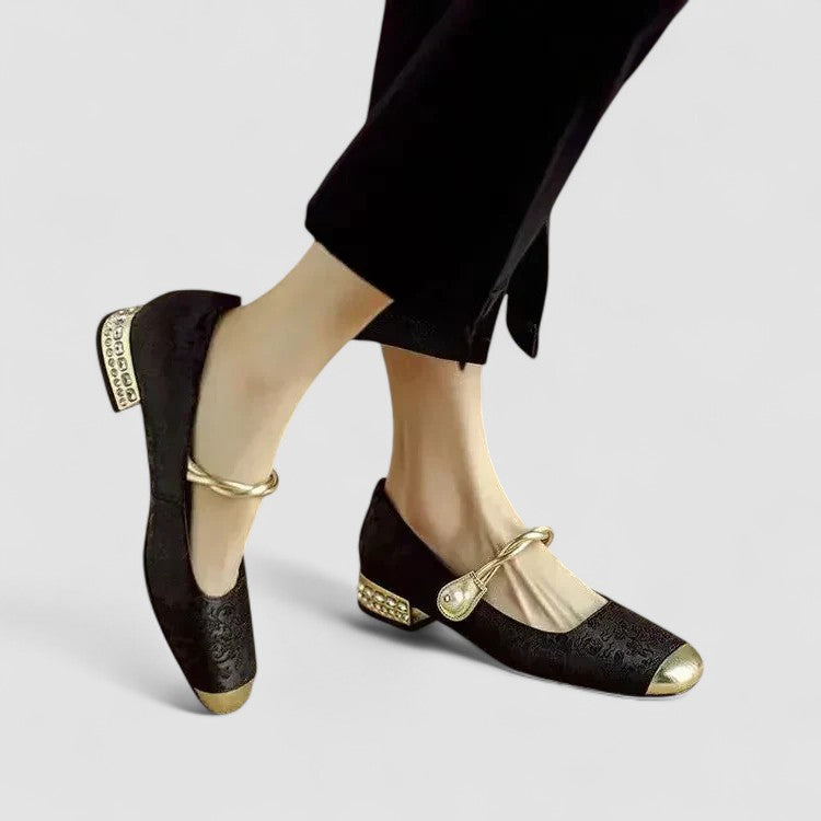 Black shoes with gold accents worn by a person on a light gray background