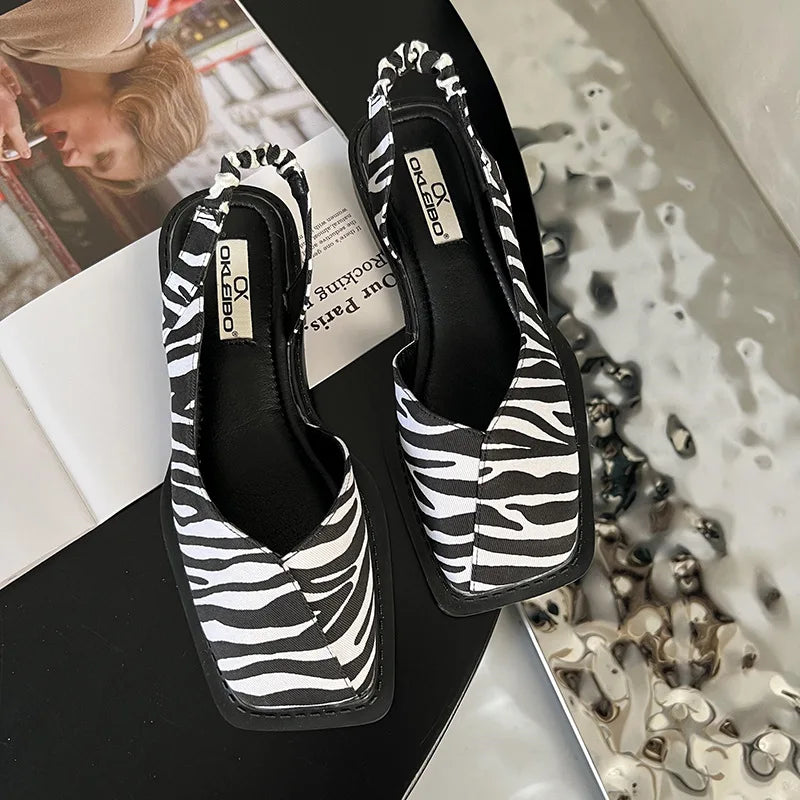 Black and white zebra patterned shoes on a surface with a magazine and puzzle pieces.