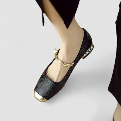 Black flat shoe with gold accents worn on a white background