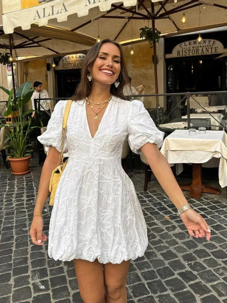 Woman in a white dress standing on a street with a restaurant in the background