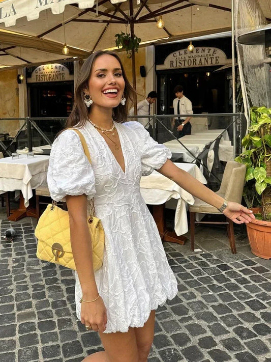 Woman in a white dress with puffed sleeves standing on a street in front of a restaurant.