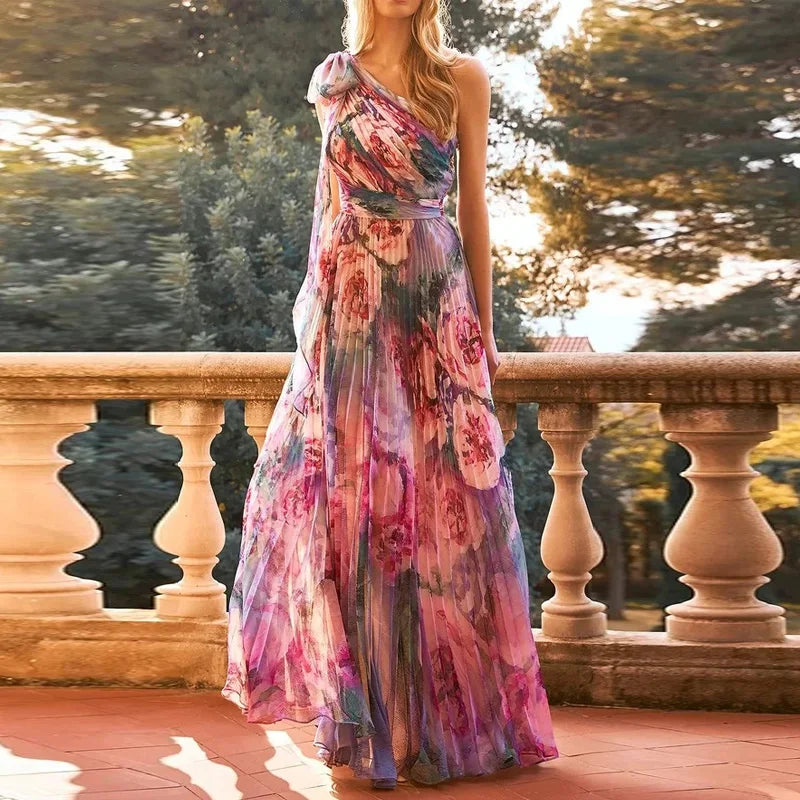 Woman wearing a floral one-shoulder dress standing on a stone path with trees in the background