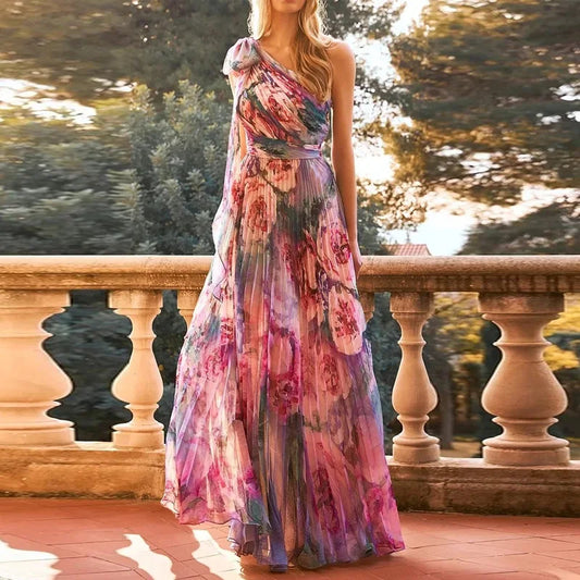 Woman wearing a floral one-shoulder dress standing on a stone path with trees in the background