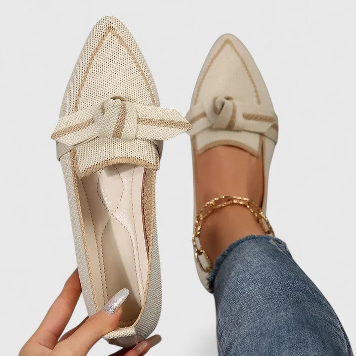Beige loafers with a bow detail worn by a person on a light gray background