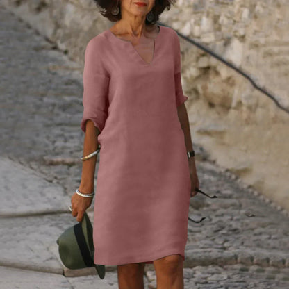 Woman wearing a pink dress standing on a stone path with a stone wall background