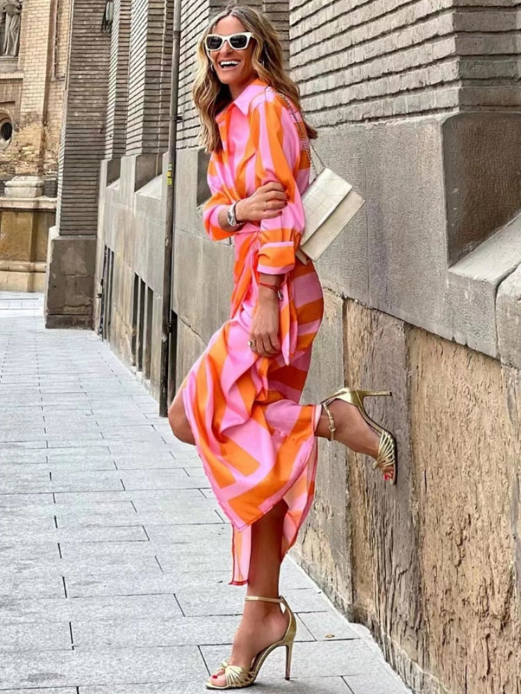 Woman in a pink and orange striped dress standing against a stone wall.