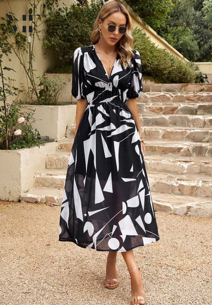 Woman wearing a black and white patterned dress standing outdoors on stone steps.