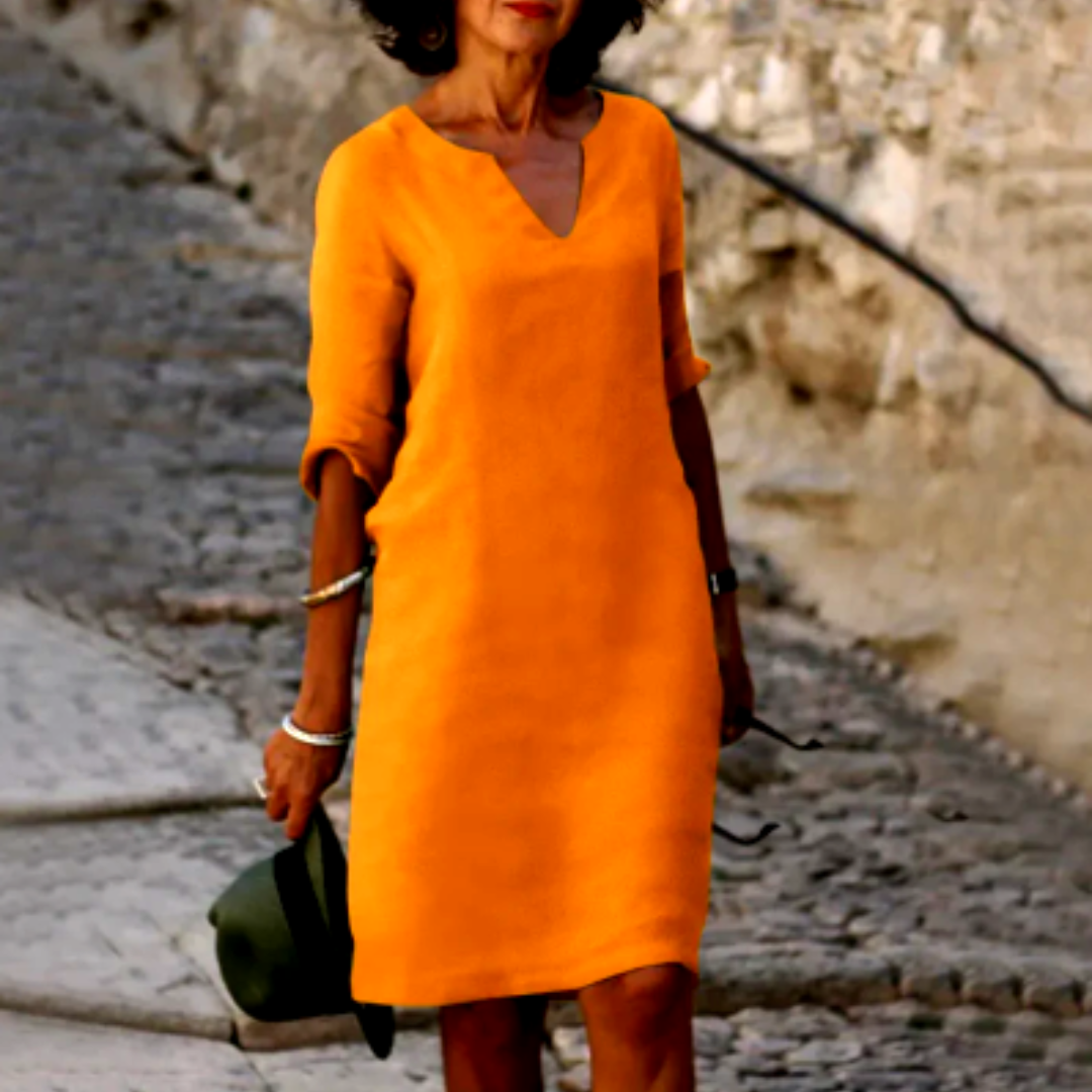 Woman wearing an orange dress holding a green hat on a stone path.