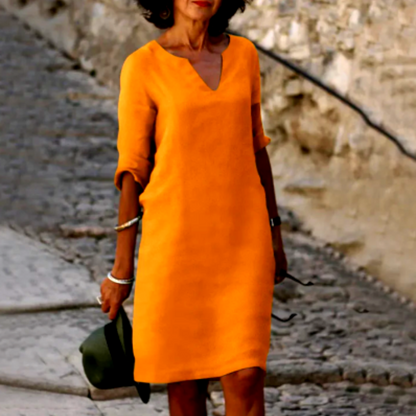 Woman wearing an orange dress holding a green hat on a stone path.