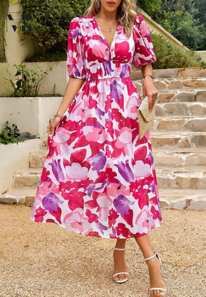 Woman wearing a pink floral dress standing on stone steps outdoors.