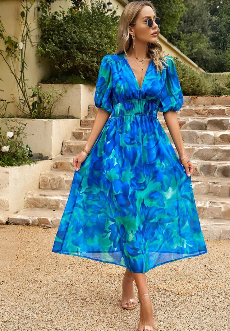 Woman wearing a blue floral dress standing on stone steps outdoors.