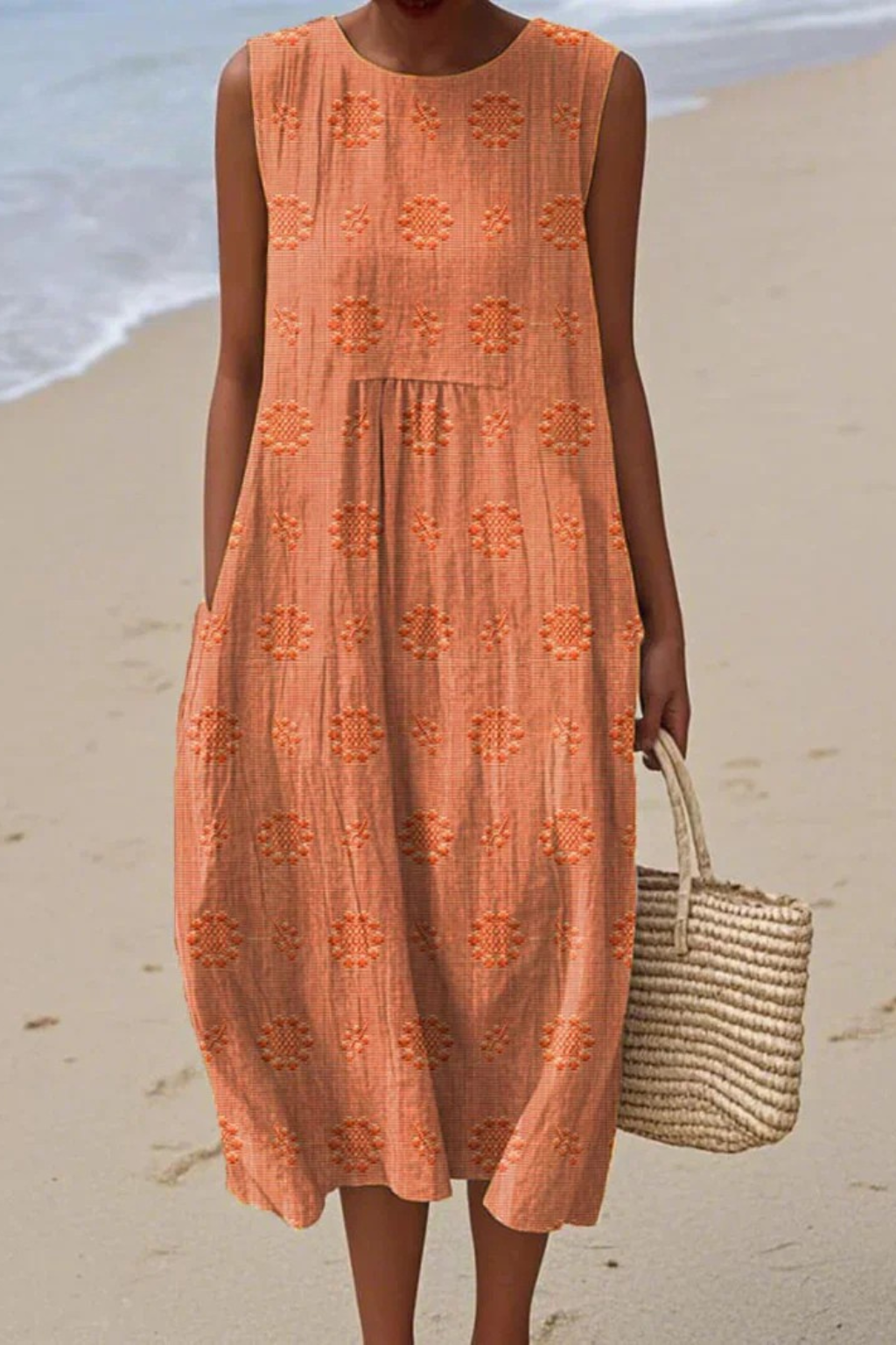 Woman in an orange dress standing on a beach with a woven bag.