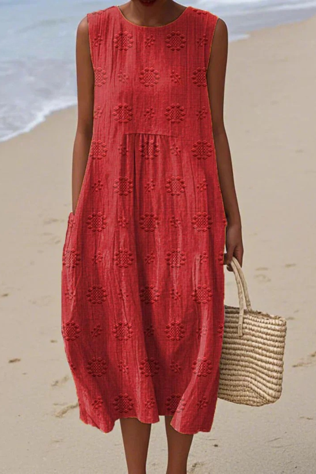 Person wearing a red dress on a beach holding a straw bag.