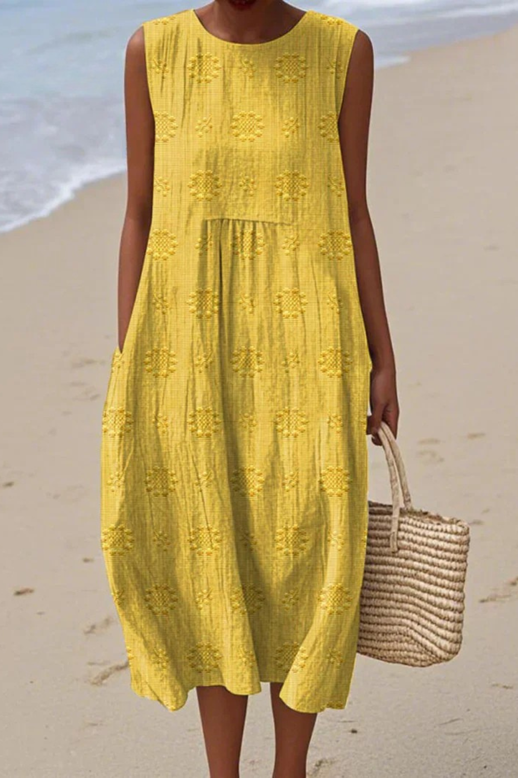 Woman in a yellow dress standing on a beach with a woven bag.