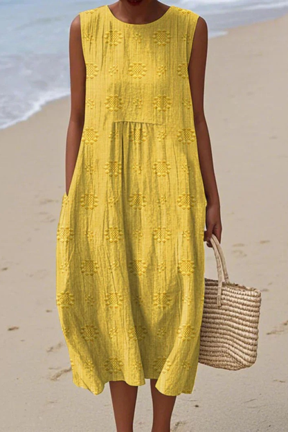 Woman in a yellow dress standing on a beach with a woven bag.