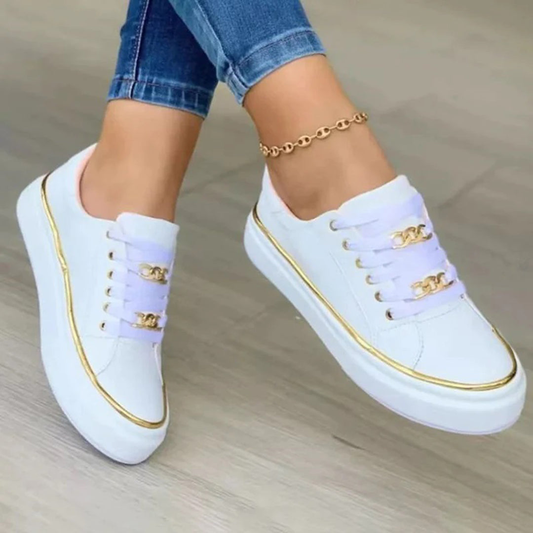 White sneakers with gold accents worn by a person on a neutral background