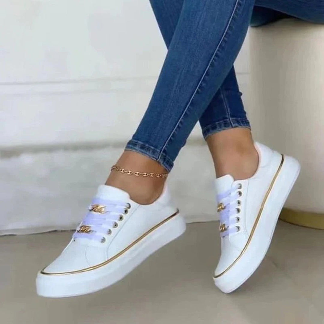 White sneakers with gold accents worn with blue jeans on a neutral background