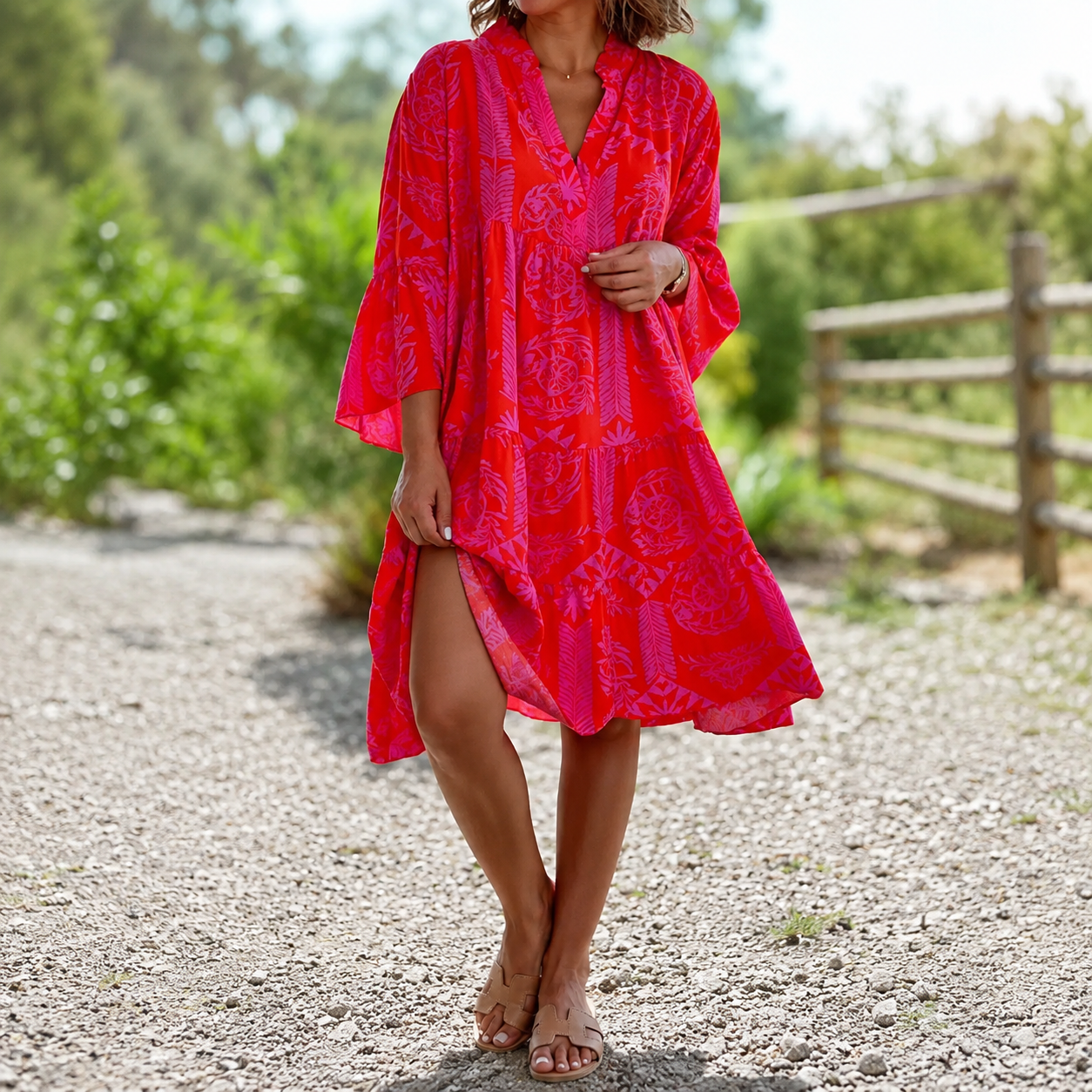 Woman wearing a bright red patterned dress standing on a gravel path with greenery in the background