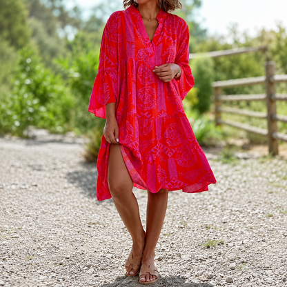 Woman wearing a bright red patterned dress standing on a gravel path with greenery in the background