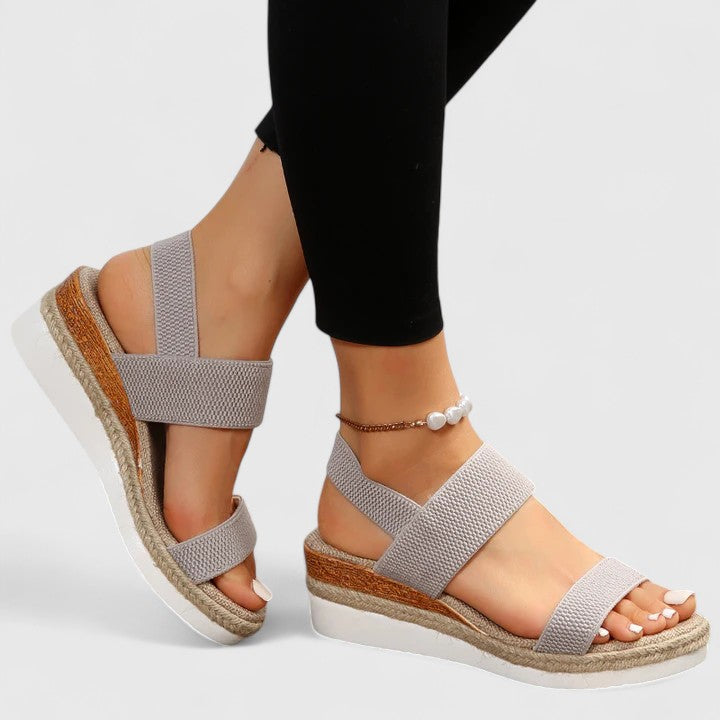 Gray wedge sandals with espadrille sole worn by a person on a light gray background