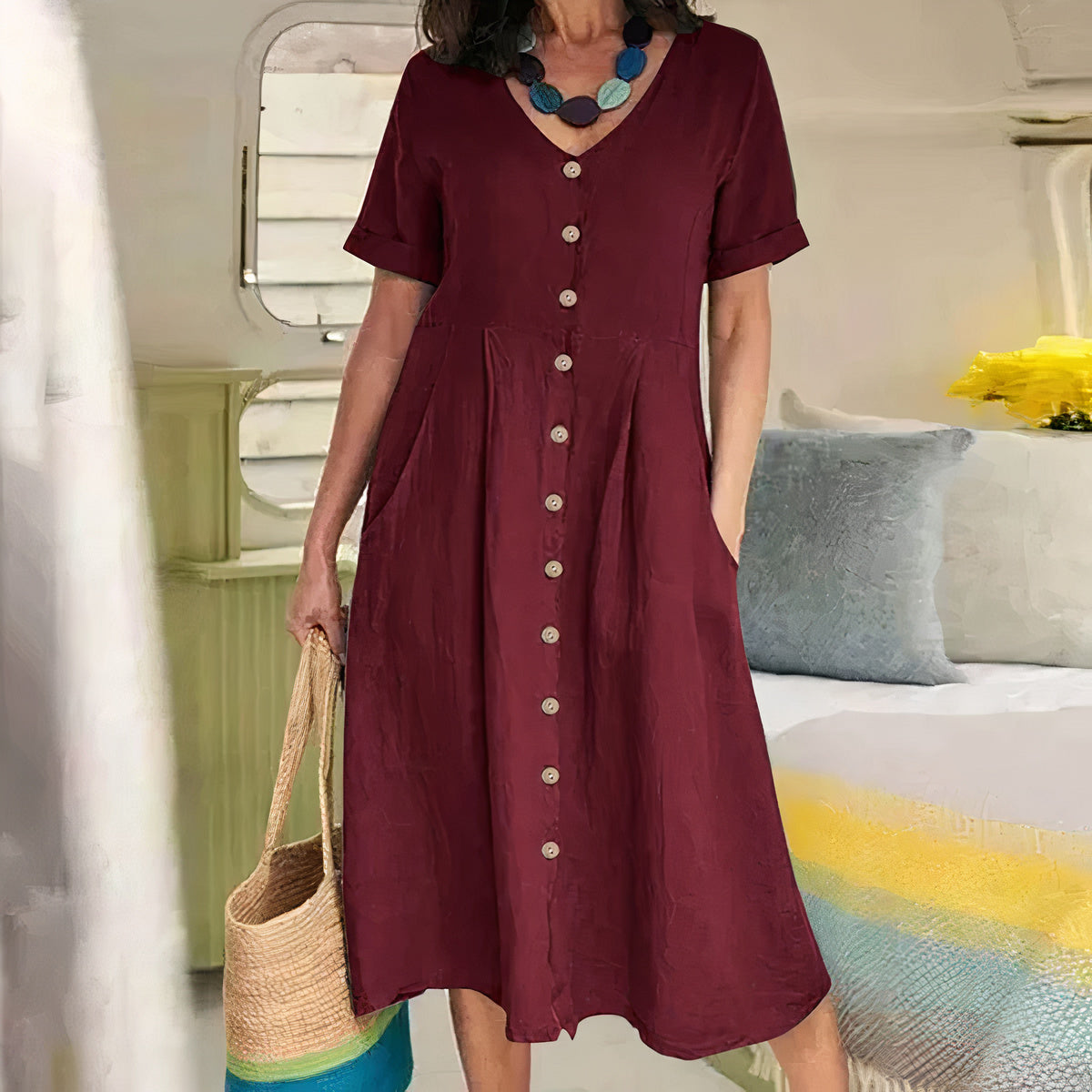 Woman wearing a burgundy dress with buttons, holding a straw bag, in an indoor setting.