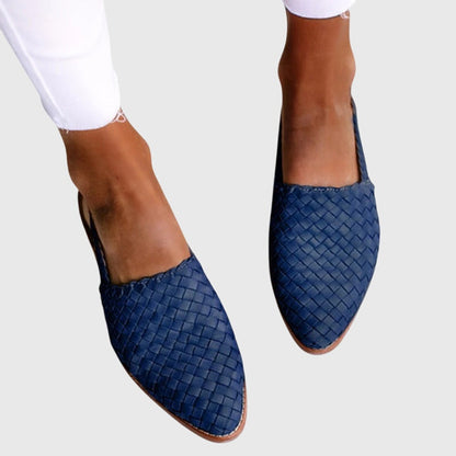 Blue woven flats worn with white pants on a light gray background