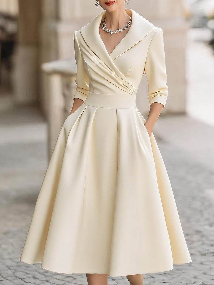 Woman wearing a cream-colored dress with a fitted bodice and full skirt on a blurred street background.