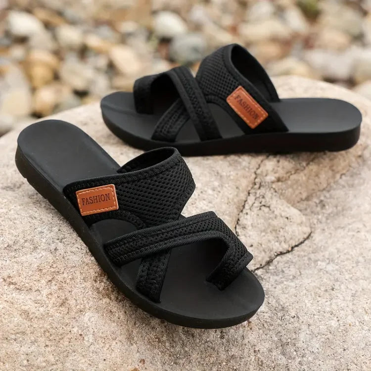 Black sandals with brown 'FASHION' labels on a stone surface