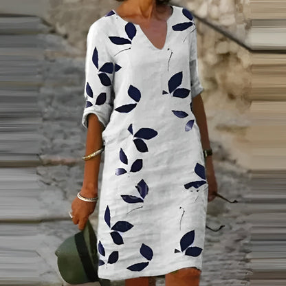 Woman wearing a white dress with blue leaf patterns, standing on stone steps.