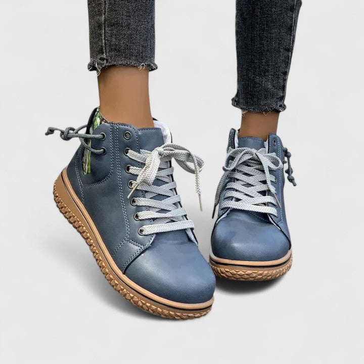 Blue leather boots with brown soles worn with rolled-up jeans on a light gray background