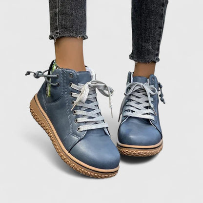 Blue leather boots with brown soles worn with rolled-up jeans on a light gray background