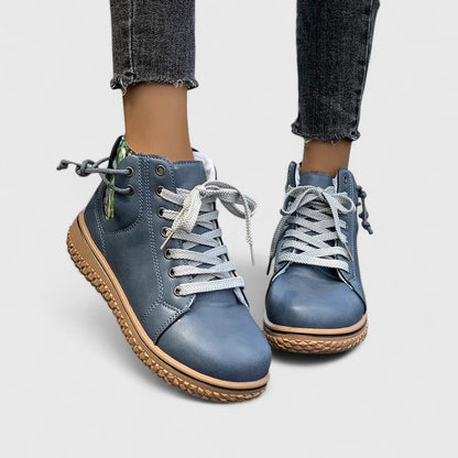Blue sneakers with brown soles worn with rolled-up jeans on a light gray background