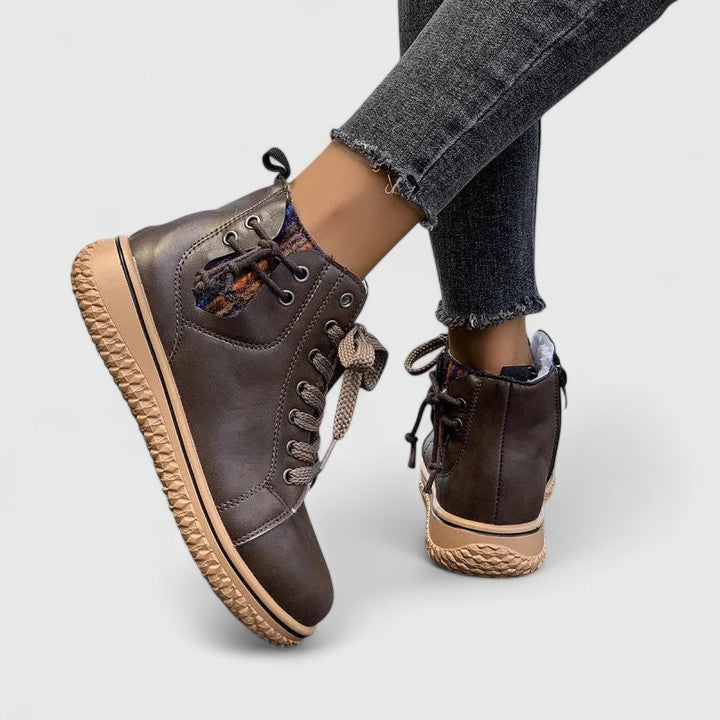 Brown leather high-top sneakers with beige soles worn by a person on a light gray background
