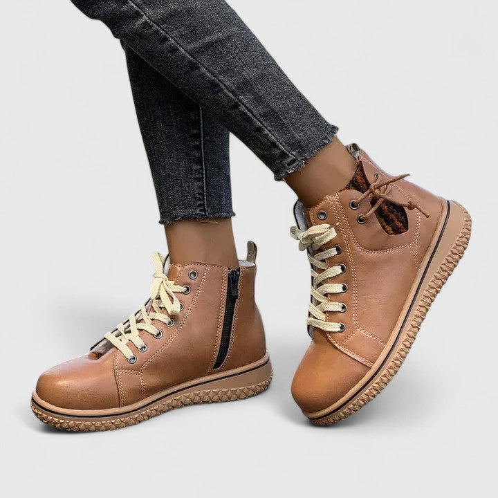 Brown leather boots with white laces worn with gray jeans on a light gray background