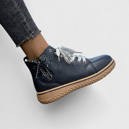 Navy blue high-top sneaker with brown sole worn by a person on a light gray background