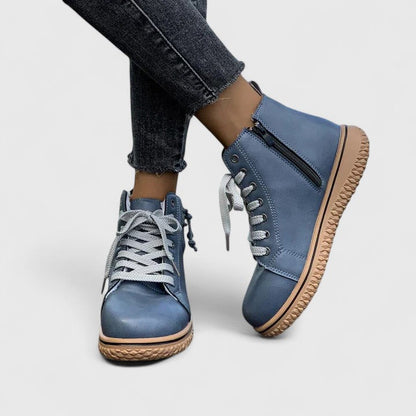 Blue sneakers with brown soles worn with dark jeans on a light gray background