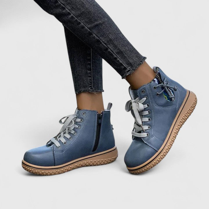 Blue boots with brown soles worn with dark jeans on a light gray background