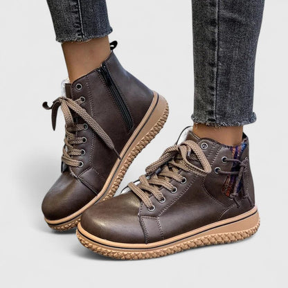 Brown leather boots with beige soles worn with jeans on a light gray background