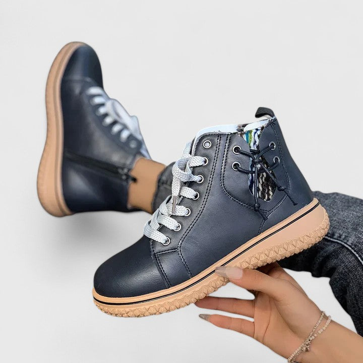 Person holding a navy blue leather boot with tan sole on a light gray background