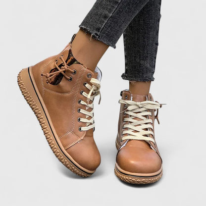 Brown leather boots with white laces worn with black jeans on a light gray background