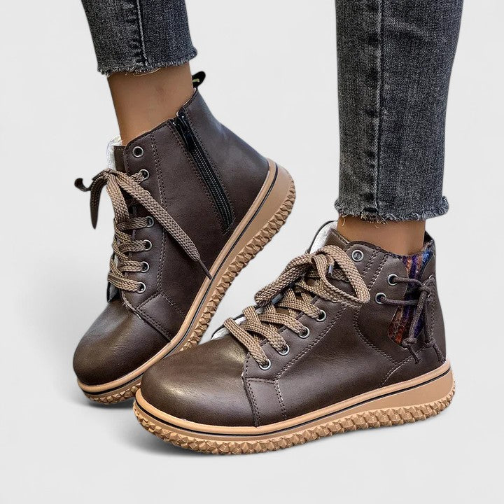 Brown leather boots with beige soles worn with jeans on a light gray background