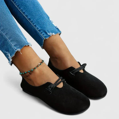 Black loafers worn with blue jeans on a neutral background