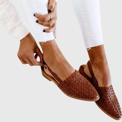 Brown woven flats worn with white pants on a light background