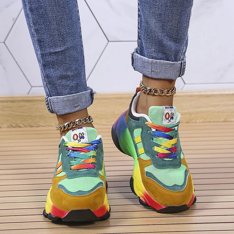 Colorful sneakers with rainbow laces worn with rolled-up jeans on a wooden floor.