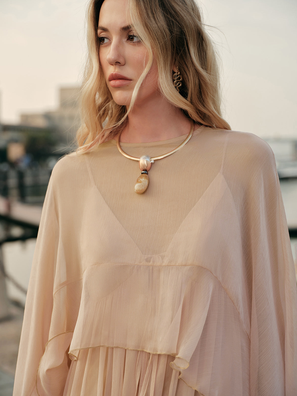 Woman wearing a beige dress with a necklace in an outdoor setting