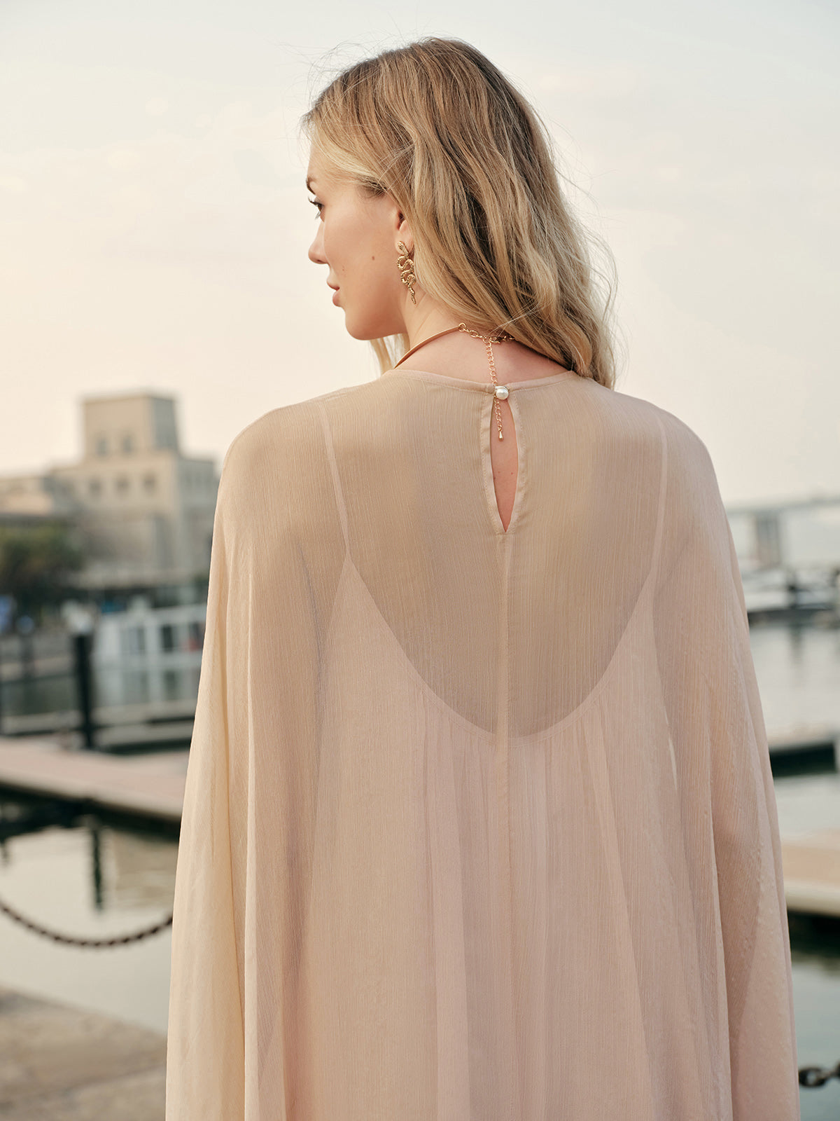 Woman wearing a sheer beige top with a cityscape in the background