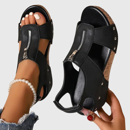 Black sandals with zippers being worn on a neutral background