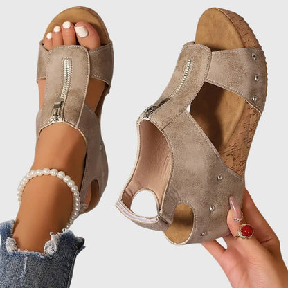 Beige wedge sandals with rhinestone embellishments worn by a person on a light gray background